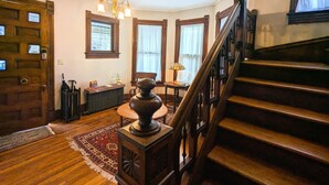 Una escalera de madera que conduce a un segundo piso, un candelabro, un radiador y una puerta con ventanal.