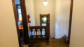 A hallway with a patterned rug, wooden staircase, a small table with a lamp, and a wall-mounted clock.