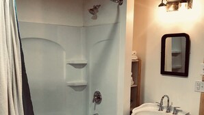 A bathroom with a bathtub, a sink, and a mirror. - Charming studio apartment in Whiteville (Whiteville)