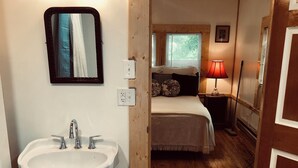 A bathroom with a pedestal sink, a mirror, and a wooden floor. - Charming studio apartment in Whiteville (Whiteville)