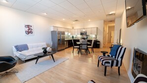 Een moderne woonkamer met een bank, salontafel en een gestreept fauteuil. In de achtergrond is een keuken met eethoek te zien.