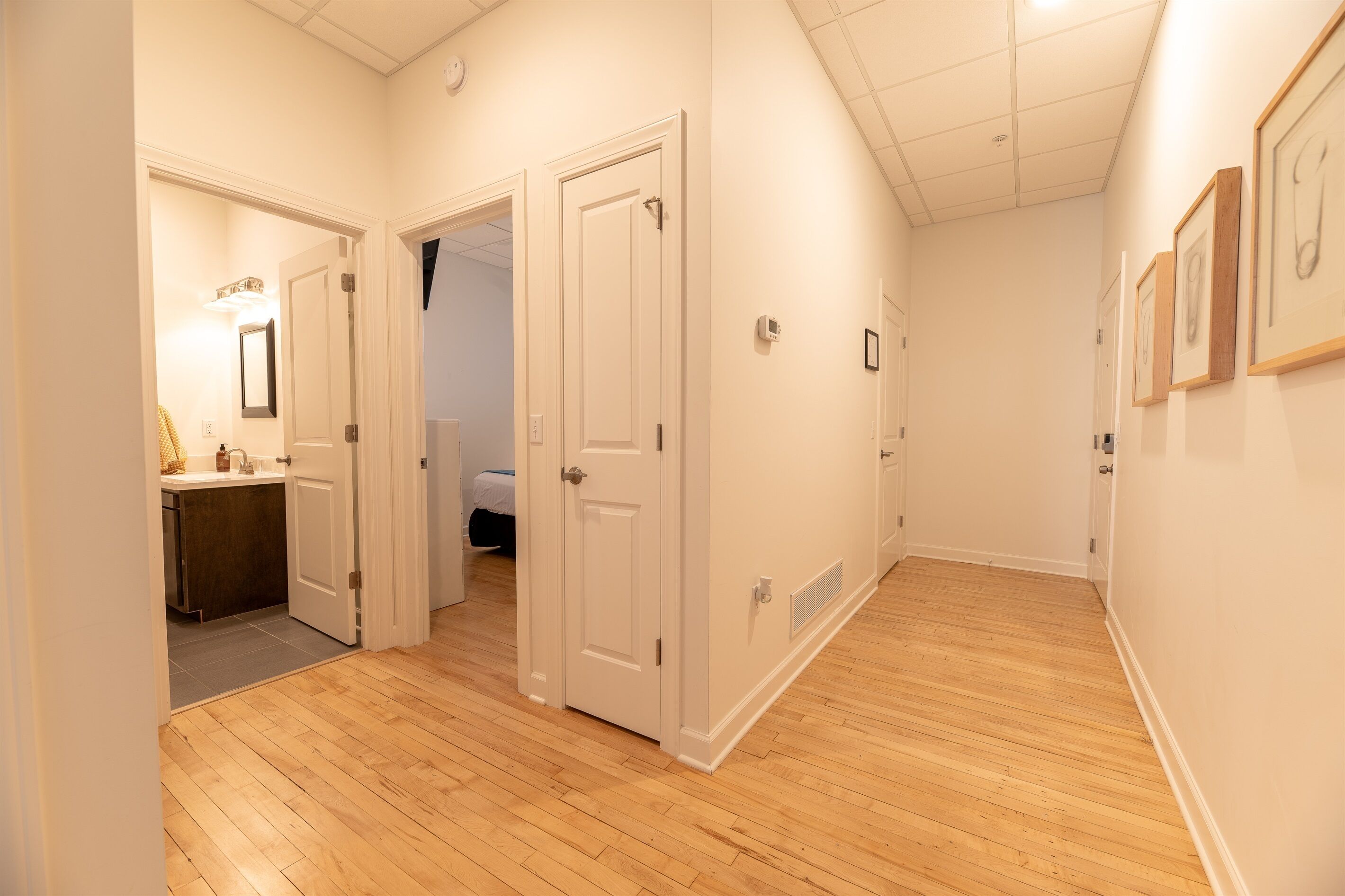 Un couloir doté d’un plancher en bois, de murs blancs et de plusieurs portes donnant sur différentes pièces.