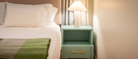 A neatly made bed with white linens, a green throw blanket, and a nightstand with a lamp.