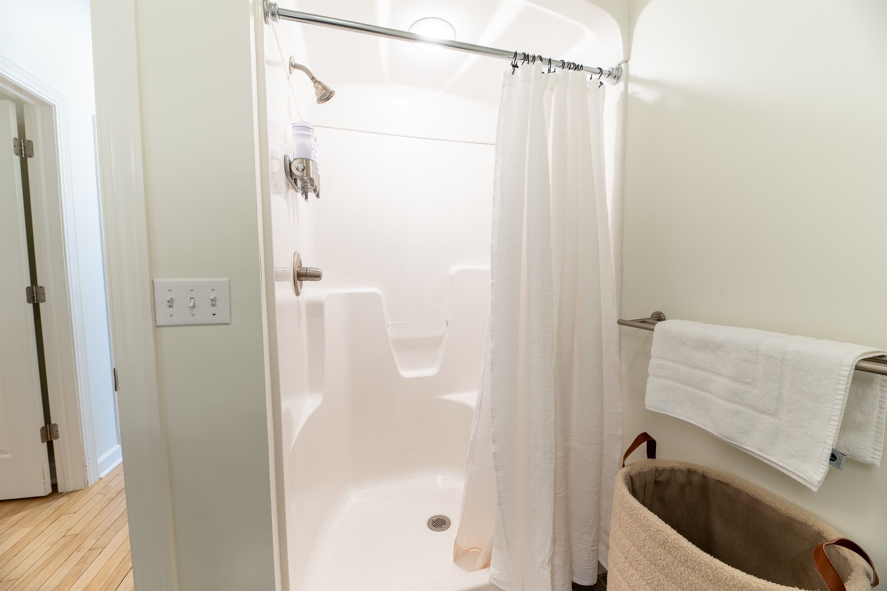 A modern bathroom with a glass-enclosed shower, a white towel rack, and a beige bath mat.