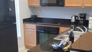 Une cuisine avec des meubles de rangement en bois, un réfrigérateur noir, un four à micro-ondes, un lave-vaisselle et une machine à café.