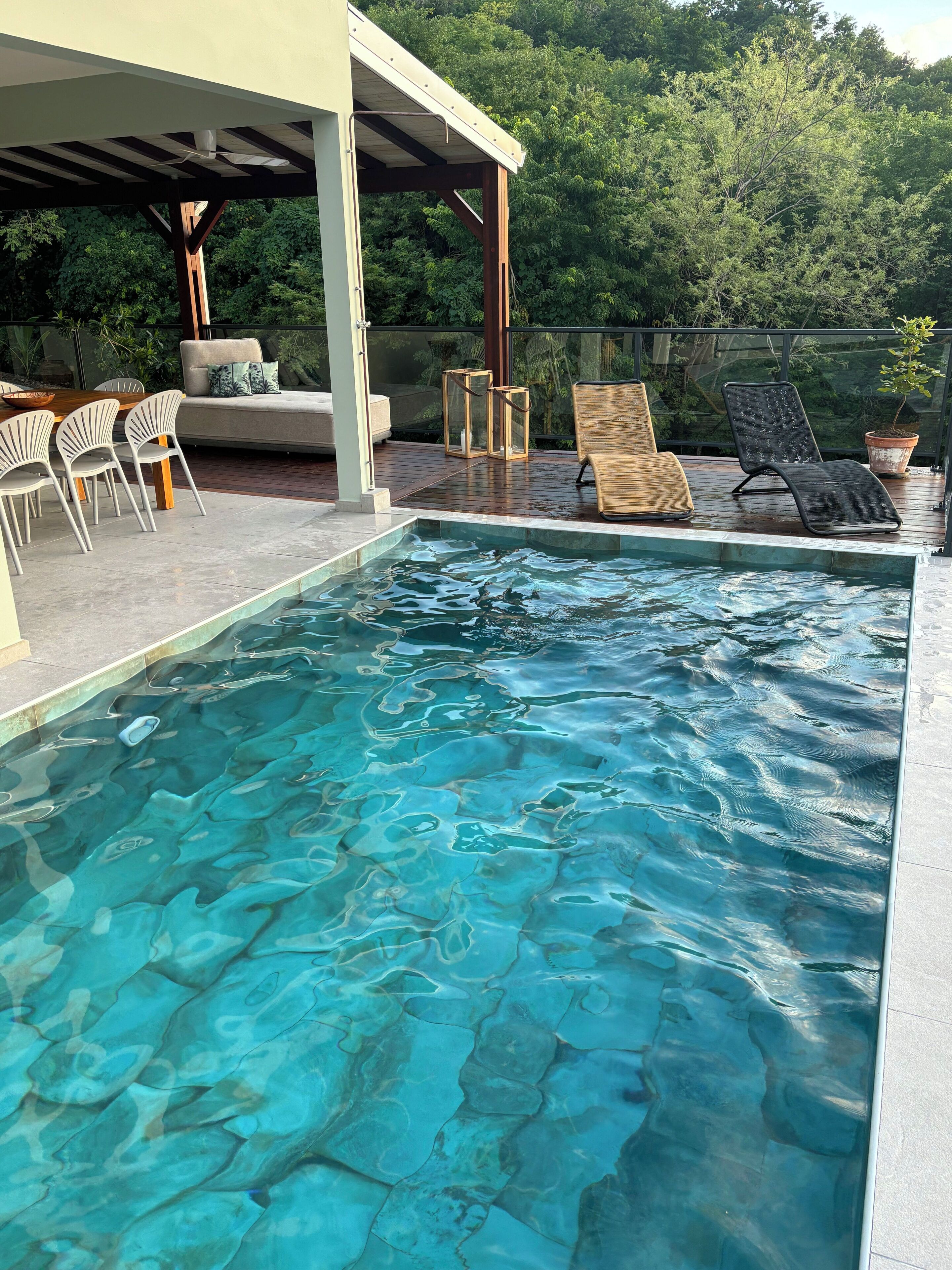 A clear swimming pool with lounge chairs and a covered seating area.