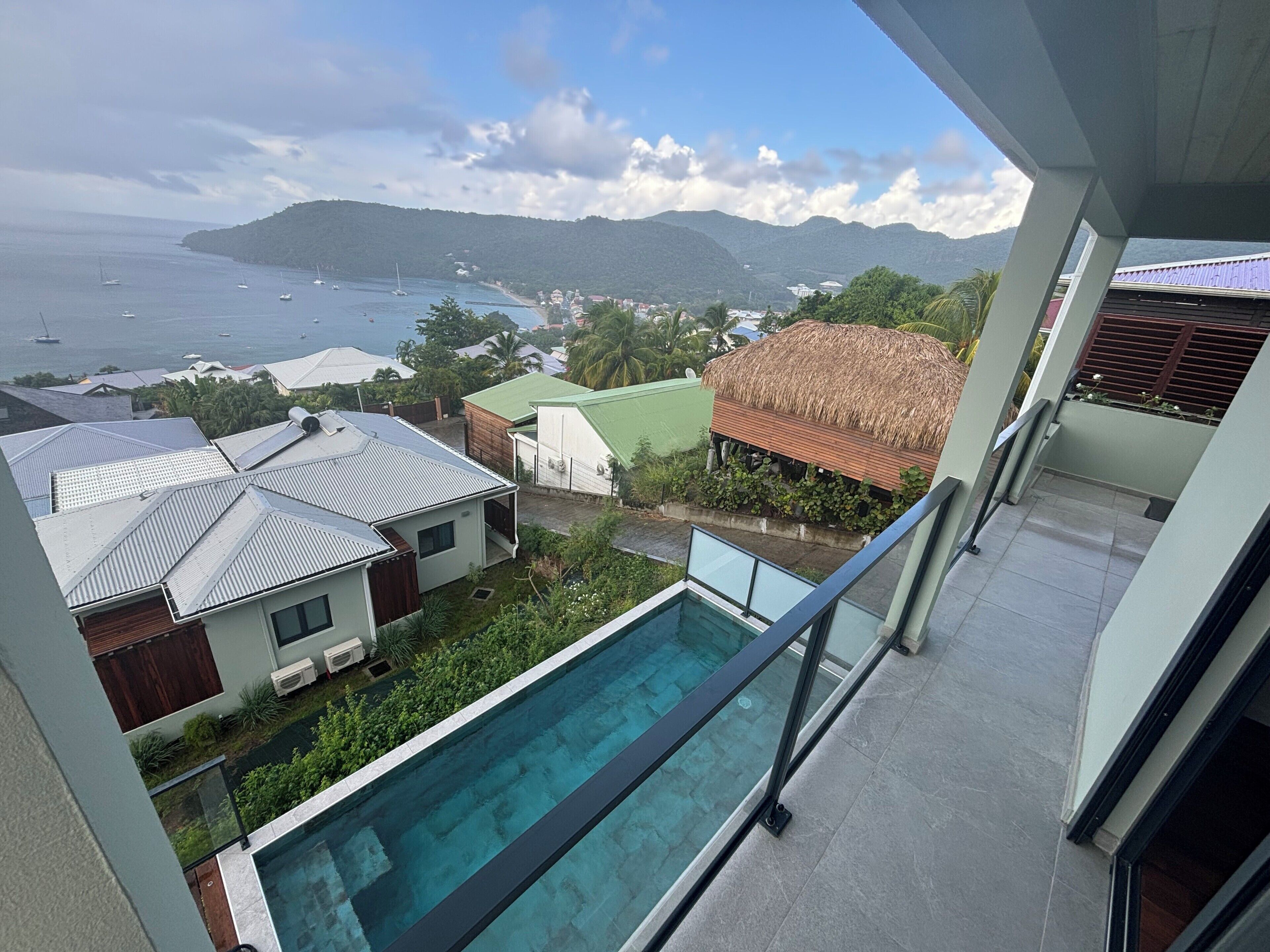 Zona residencial con piscina, casas de techo metálico y vistas al mar y a las montañas.