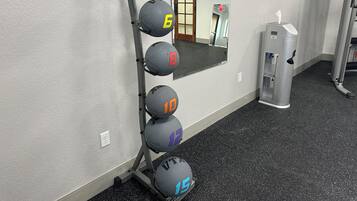 Ett gym med ett väggmonterat ställ för vikter, där det finns fem träningsbollar, en spegel och en vattenautomat.