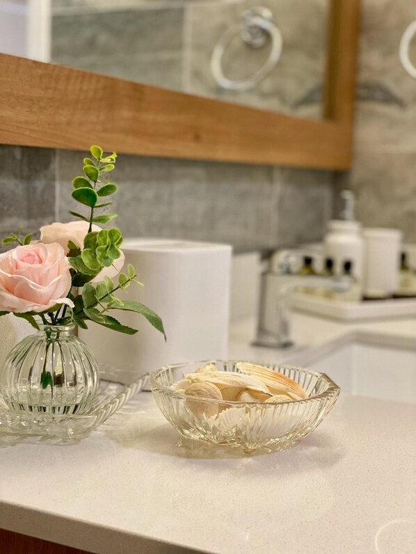 A bathroom vanity with a glass vase containing a pink rose and a bowl of bananas. - B&J HOTELS (Roswell)