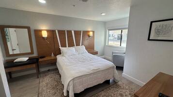 A hotel room with a large bed, bedside tables, a desk, a chair, and a window.