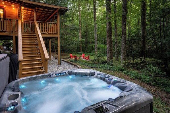 Un bain à remous entouré d’une terrasse en bois et d’une forêt.