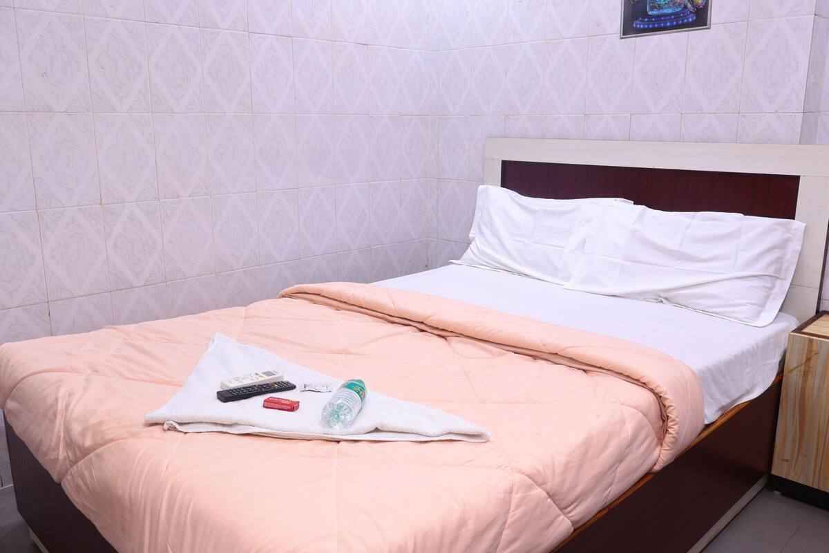 Una cama bien tendida con una manta color melocotón, almohadas blancas y una toalla blanca doblada encima.