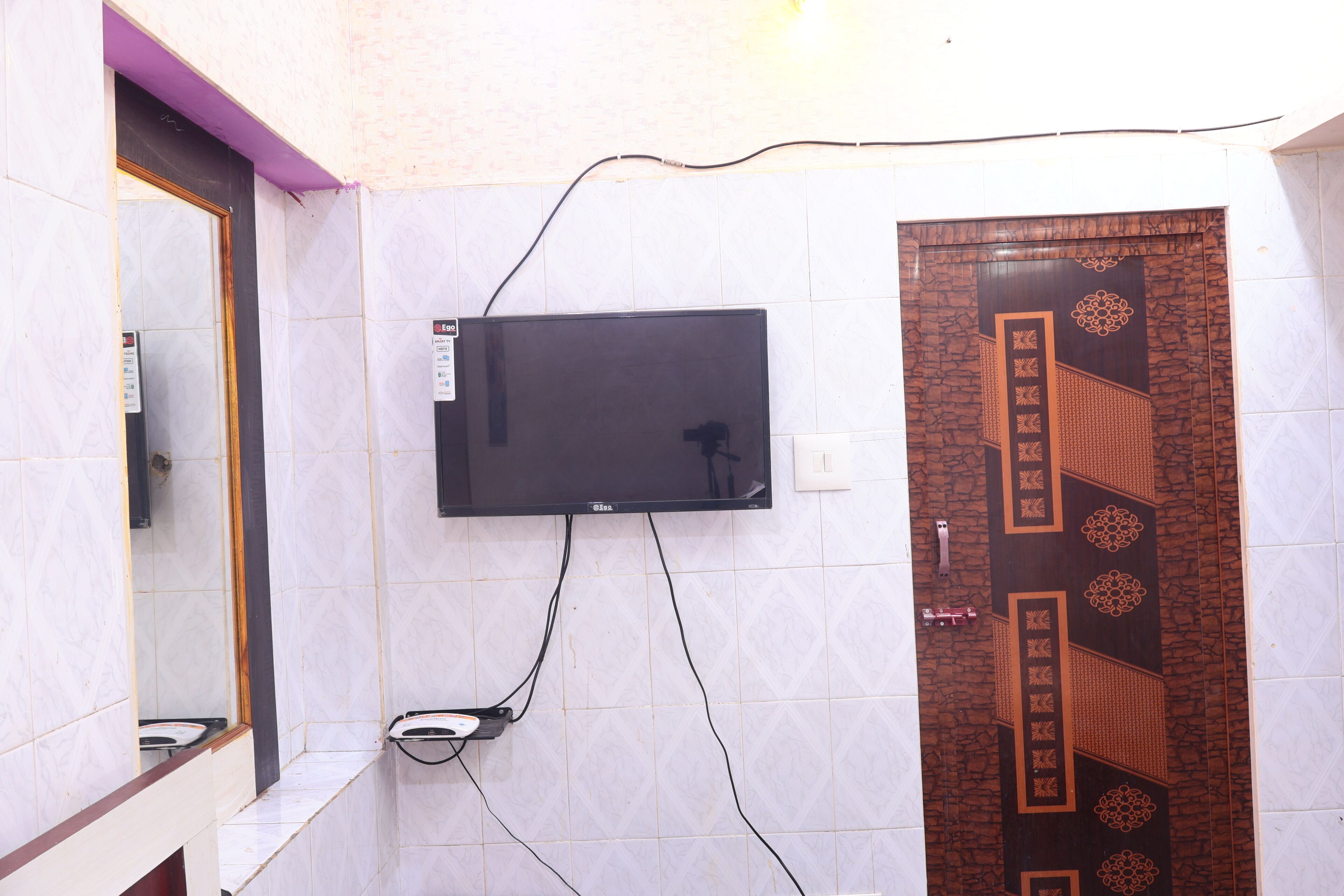 Een badkamer met een tv aan de muur, een spiegel en een decoratieve deur.