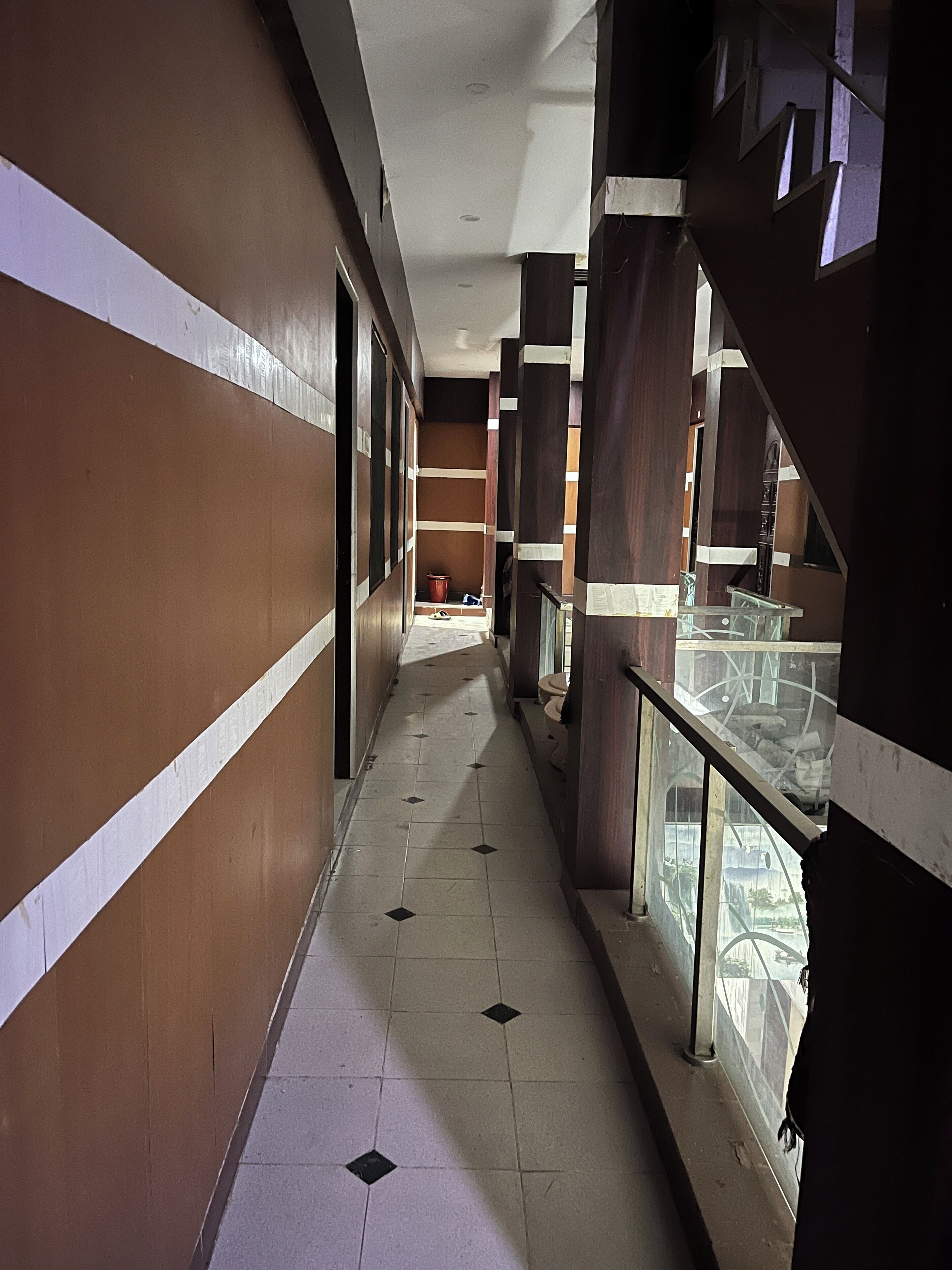 A corridor with tiled flooring, wooden paneling, and glass railings.
