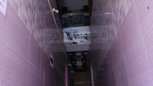 Un couloir étroit aux murs recouverts de carreaux violets et un escalier menant à un niveau inférieur.