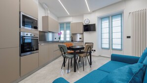 Et moderne køkken med indbyggede apparater, et spiseområde med bord og stole, og en blå sofa.