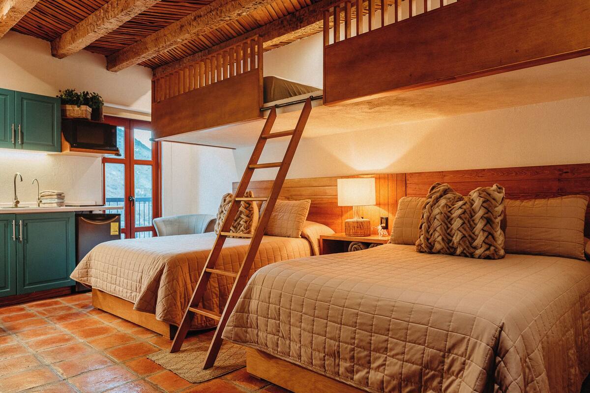 A cozy bedroom with two beds, a ladder, a desk, and a window.