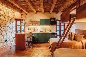 A cozy room with a bed, a wooden ladder, a stone wall, and a kitchen area with green cabinets and a wooden ceiling. - Villa Mosaico (Real de Catorce)