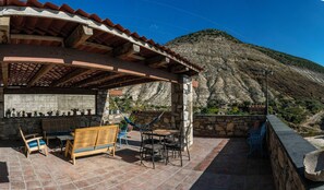 A covered outdoor seating area with stone walls, wooden furniture, and a view of a mountainous landscape. - Villa Mosaico (Real de Catorce)