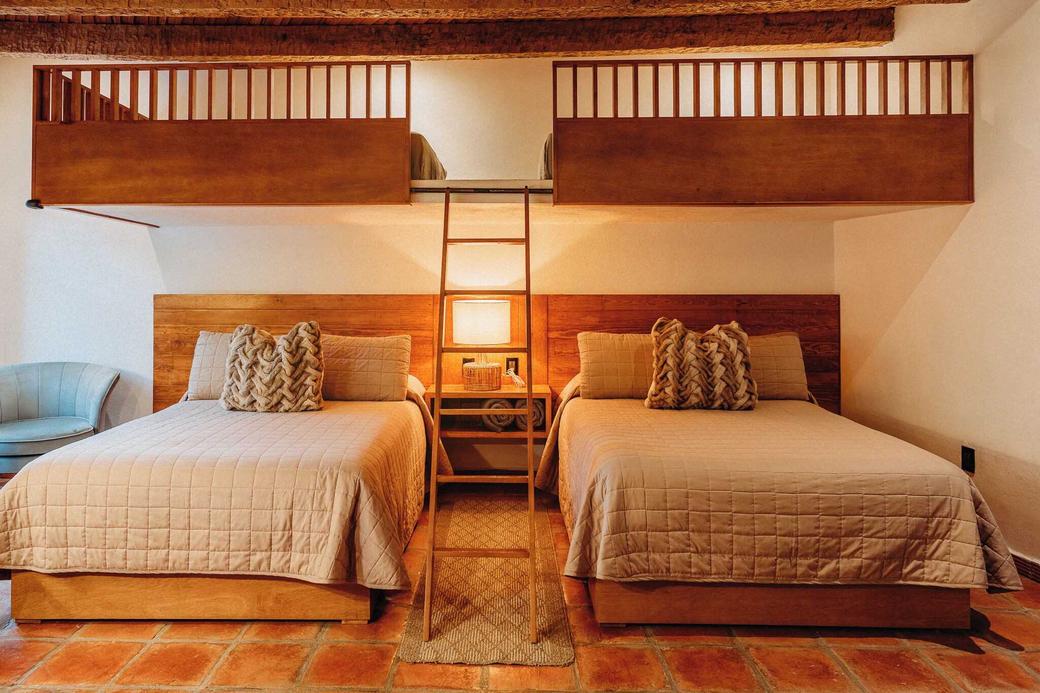Una habitación con dos camas, una escalera, una silla y una mesita de noche con lámpara.