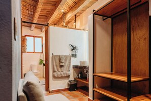 Un baño con techo de madera, una toalla colgada en la pared, un inodoro y una pequeña estantería con una planta.