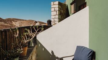 A balcony with a wicker chair and a small table, a potted plant, and a view of the hills.