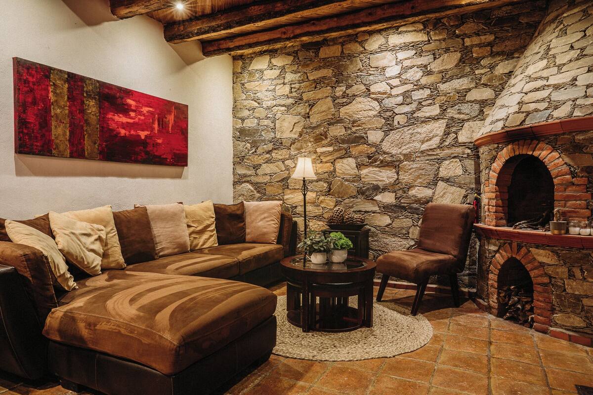 A cozy living room with a stone wall, a fireplace, a sofa, and a lamp.