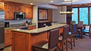 Una cocina moderna con armarios de madera, encimera de granito, microondas integrado y una zona de bar con taburetes.
