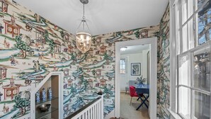 A hallway with traditional Asian-style wallpaper, a wooden staircase, and a dining area with a red chair. - Spacious 1BR on Salem Common l Steps to Downtown l Fenced in Yard + Parking (Salem)