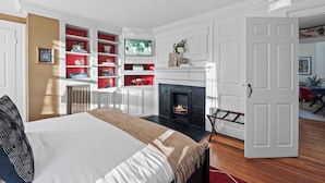 A bedroom with a bed, a fireplace, and built-in shelving with books and decorative items. - Spacious 1BR on Salem Common l Steps to Downtown l Fenced in Yard + Parking (Salem)