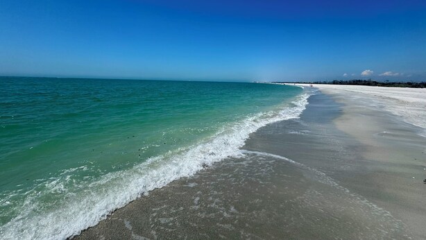 Een strand met helder turquoise water en een breed zandstrand.