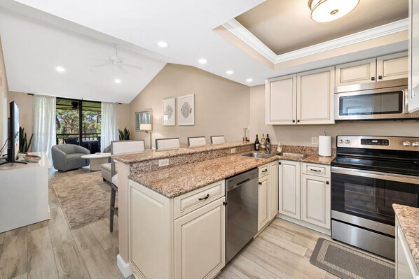 A modern kitchen with granite countertops, stainless steel appliances, and a dining area with a gray sofa.