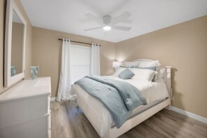 Ein Schlafzimmer mit einem Bett, einem Deckenventilator, einem Fenster mit Vorhängen und einem Nachttisch.