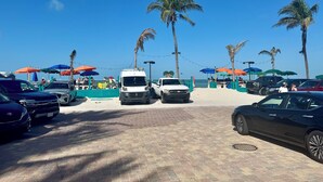 Een parkeerplaats aan het strand met voertuigen, palmbomen en strandparasols.