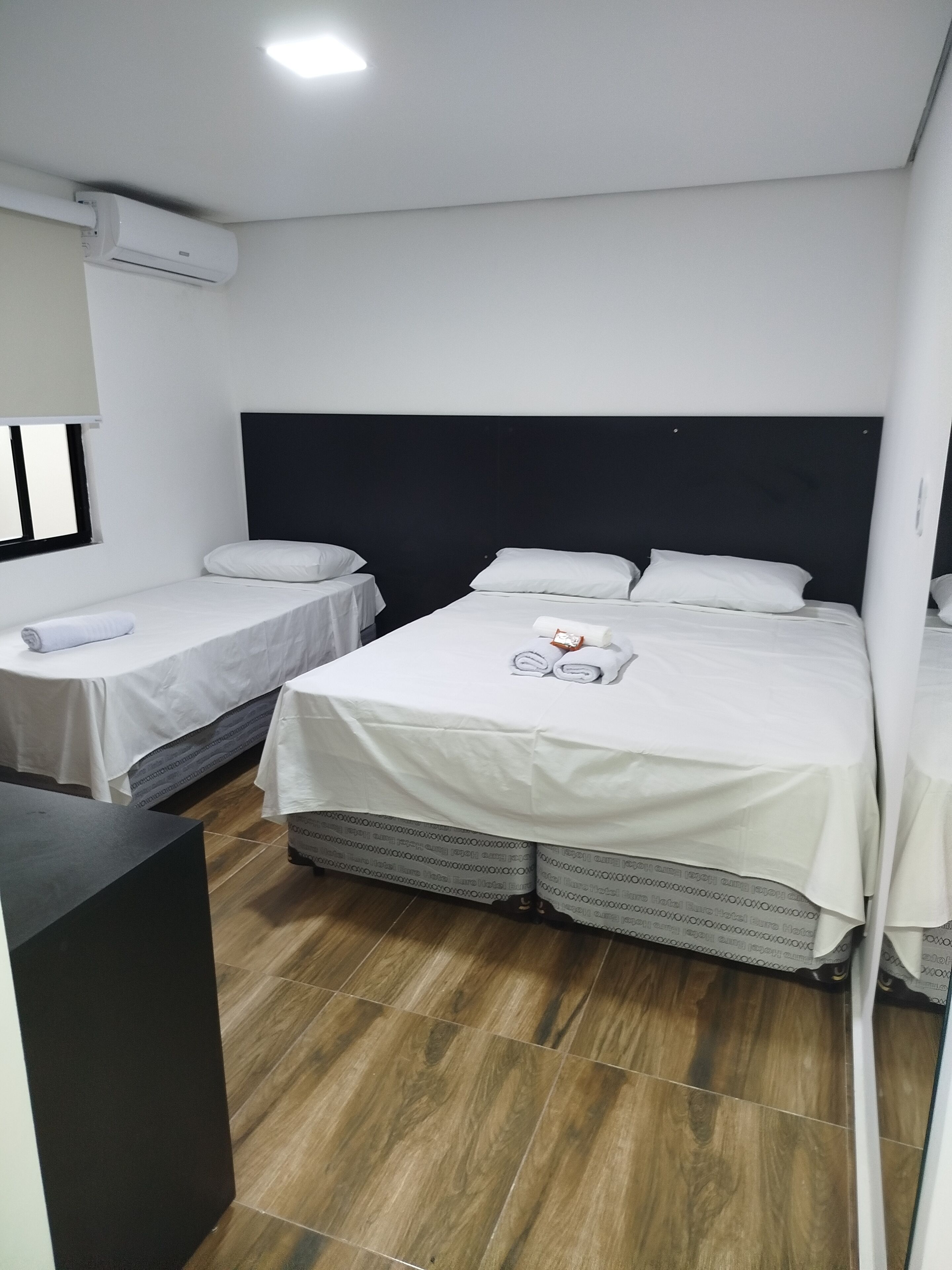 Una habitación de hotel con dos camas individuales, una cama grande, un escritorio y una ventana.