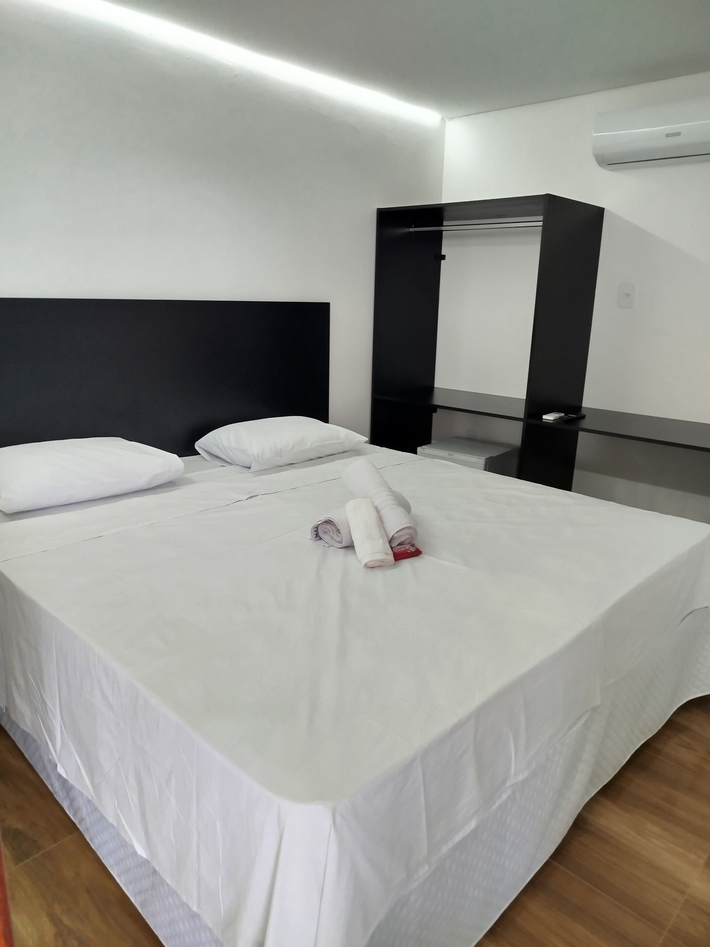 Et hotelværelse med en pænt redt seng, en sort sengegavl, et spejl og en hvid aircondition-enhed på væggen.