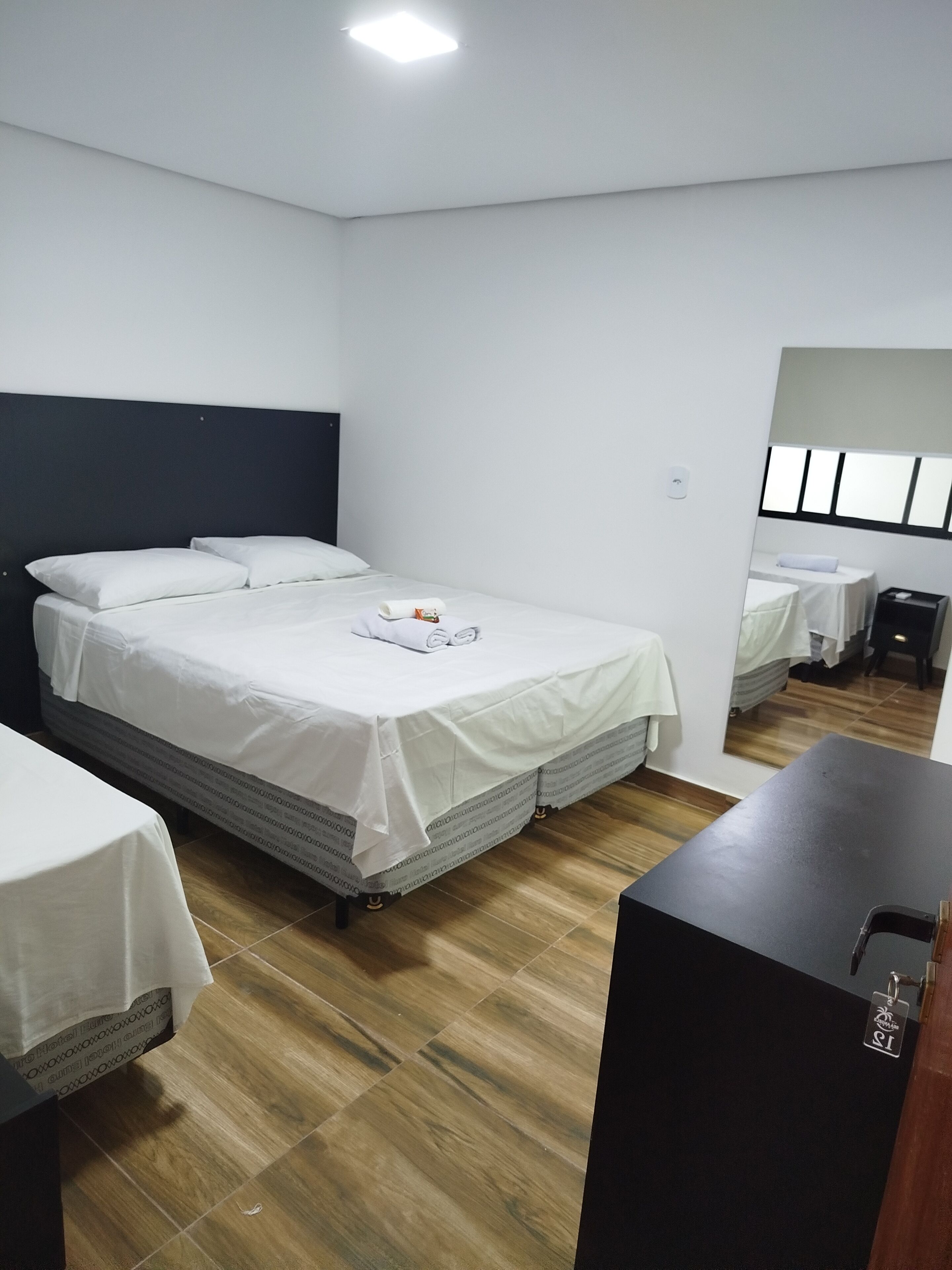 Quarto de hotel com uma cama grande, uma cama menor, uma escrivaninha e um espelho.