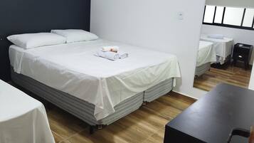 Quarto de hotel com uma cama grande, uma cama menor, uma escrivaninha e um espelho.