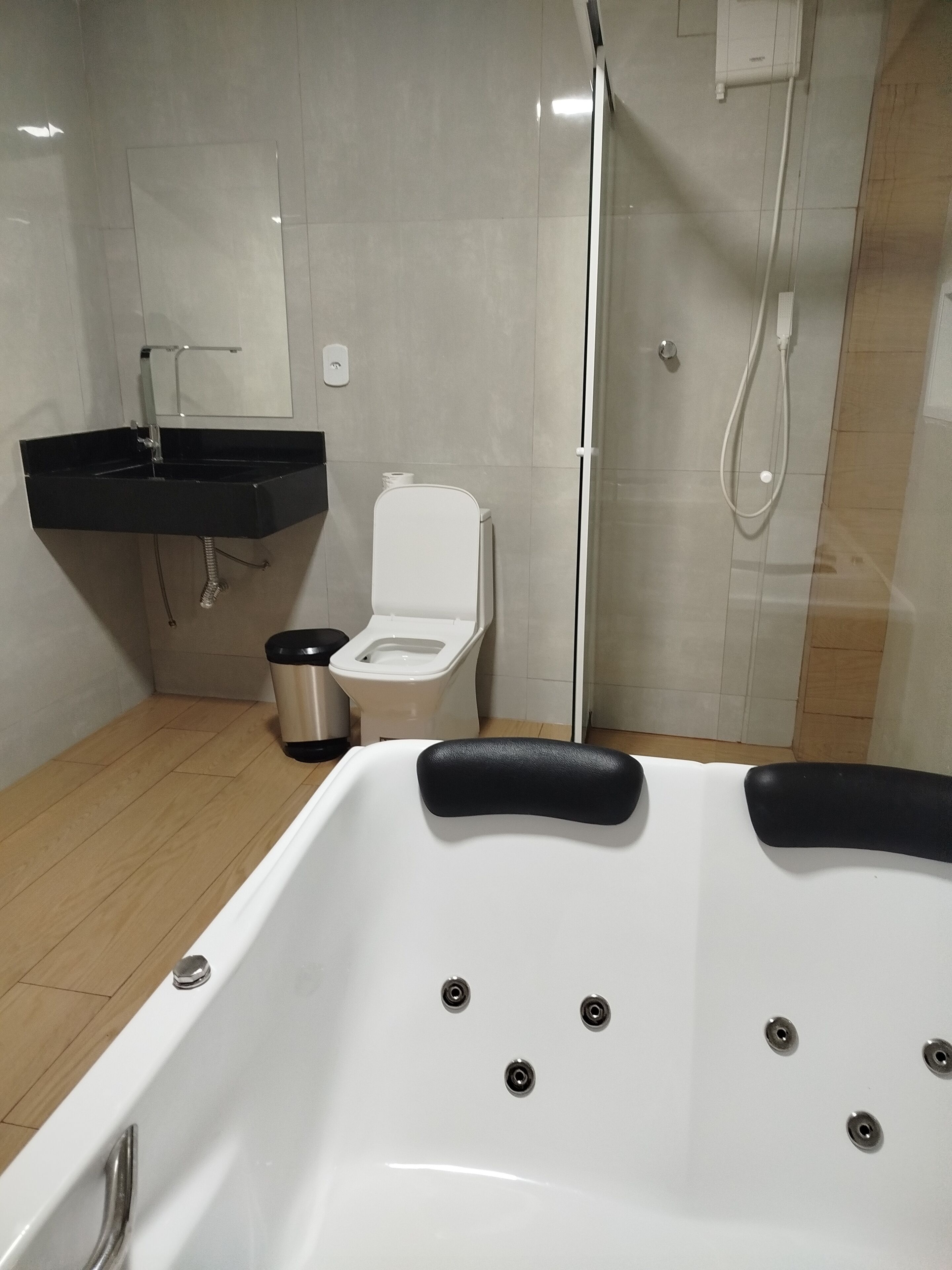 Un bany modern amb una banyera blanca, un lavabo negre, un vàter i un box de dutxa de vidre.
