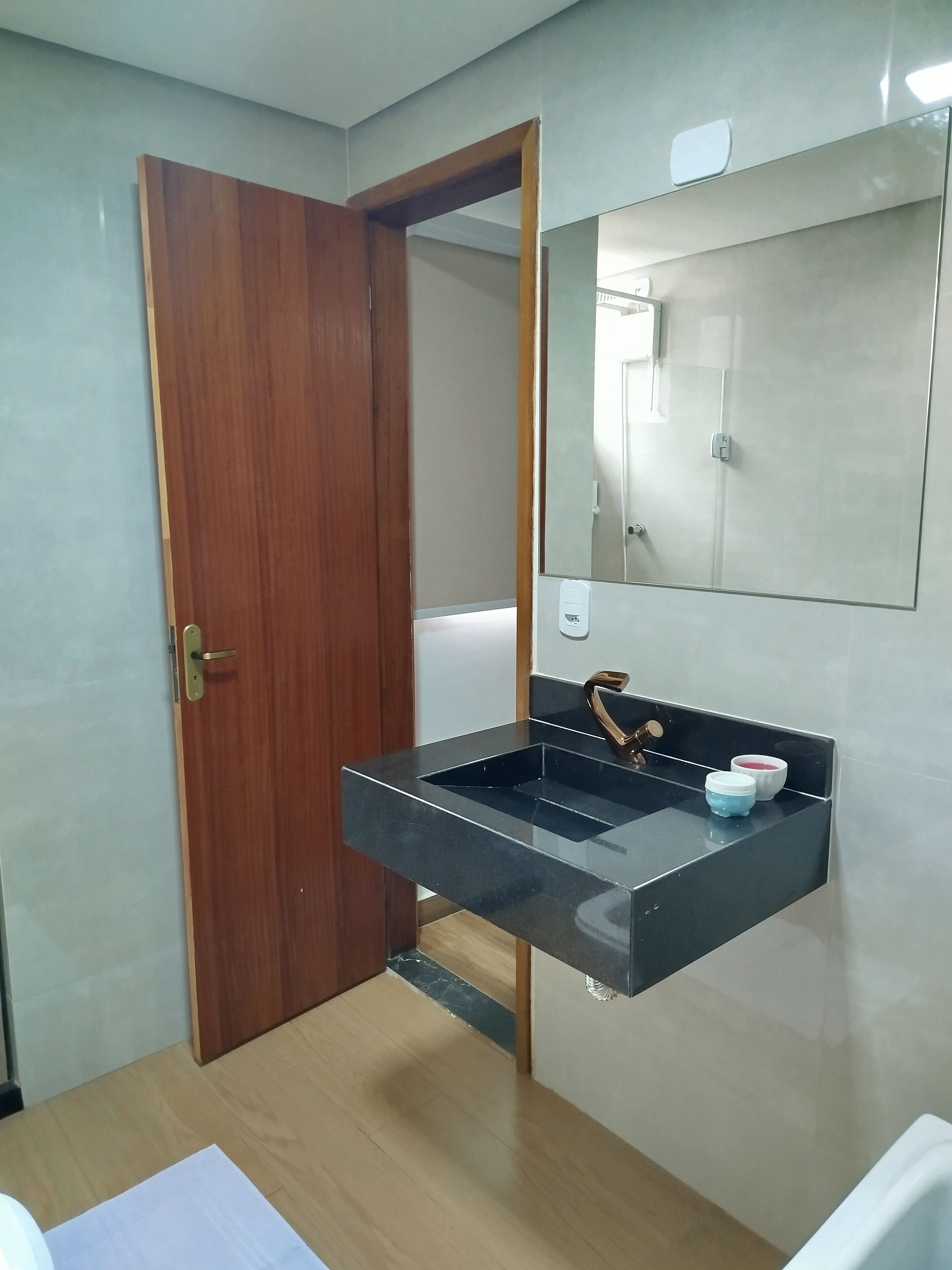 A bathroom with a wooden door, a black sink with a mirror above it, and a small shelf with two containers.