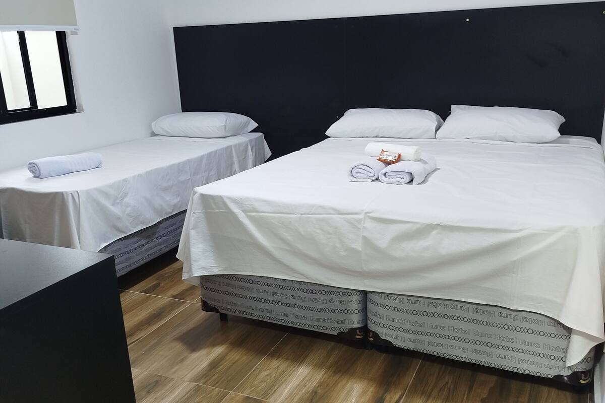A hotel room with two single beds, a large bed, a desk, and a window.
