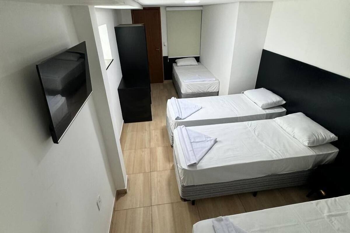 A compact hotel room with two single beds, a flat-screen TV mounted on the wall, and a wooden door.