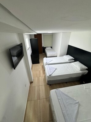 Une chambre d’hôtel compacte, dotée de deux lits simples, d’un téléviseur à écran plat fixé au mur et d’une porte en bois.