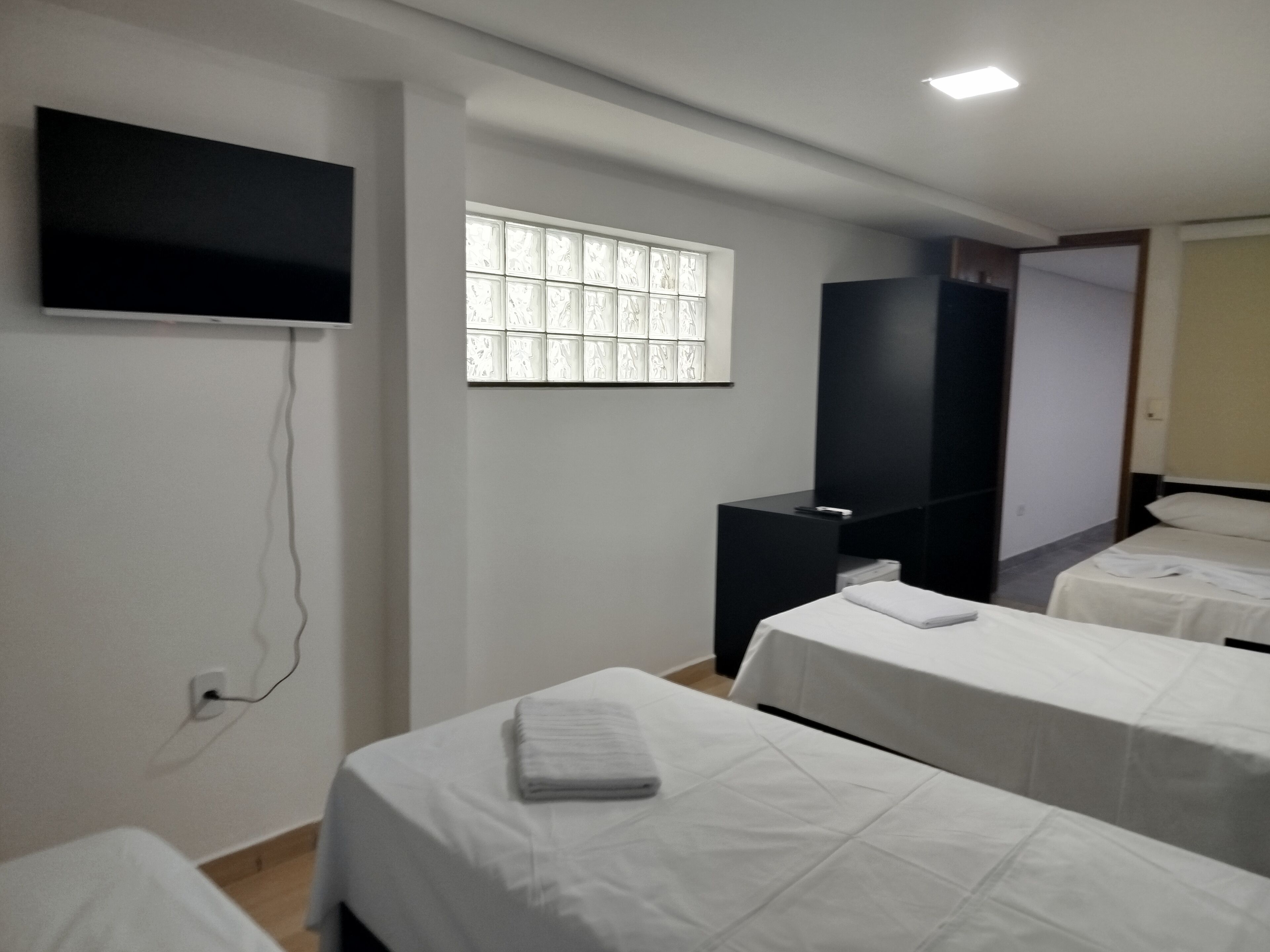A hotel room with two beds, a flat-screen TV mounted on the wall, a wardrobe, and a window with frosted glass panels.
