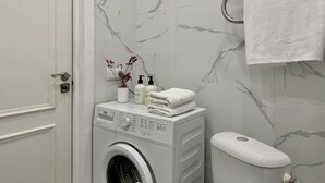 A modern bathroom with a washing machine, toiletries, and a toilet. - Cozy studio with WiFi and AC in center of Almaty (Almaty)