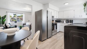 A modern kitchen with white cabinets, stainless steel appliances, and a dining area with a dark table and chairs. - NEW Tranquil Escape - Hot Tub, BBQ, Near LA & Disney (Covina)
