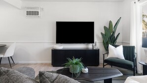 A modern living room with a flat-screen TV mounted on a black console, a large green plant, and a dark coffee table. - NEW Tranquil Escape - Hot Tub, BBQ, Near LA & Disney (Covina)