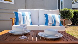A wooden table with two white plates and two wine glasses, set in front of a white sofa with blue pillows. - NEW Tranquil Escape - Hot Tub, BBQ, Near LA & Disney (Covina)