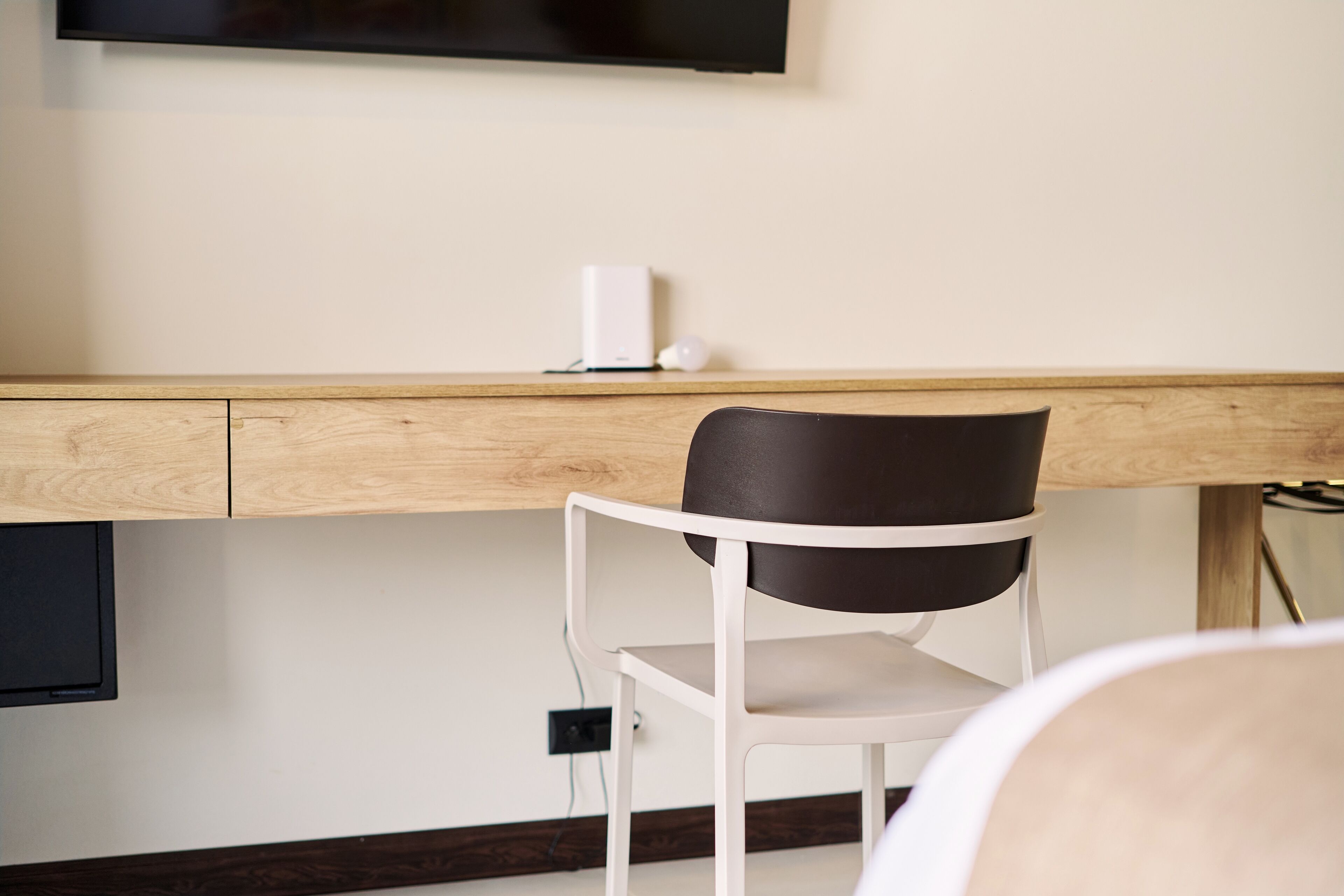 Una habitación moderna con un escritorio de madera, una silla blanca y un televisor de pantalla plana en la pared.