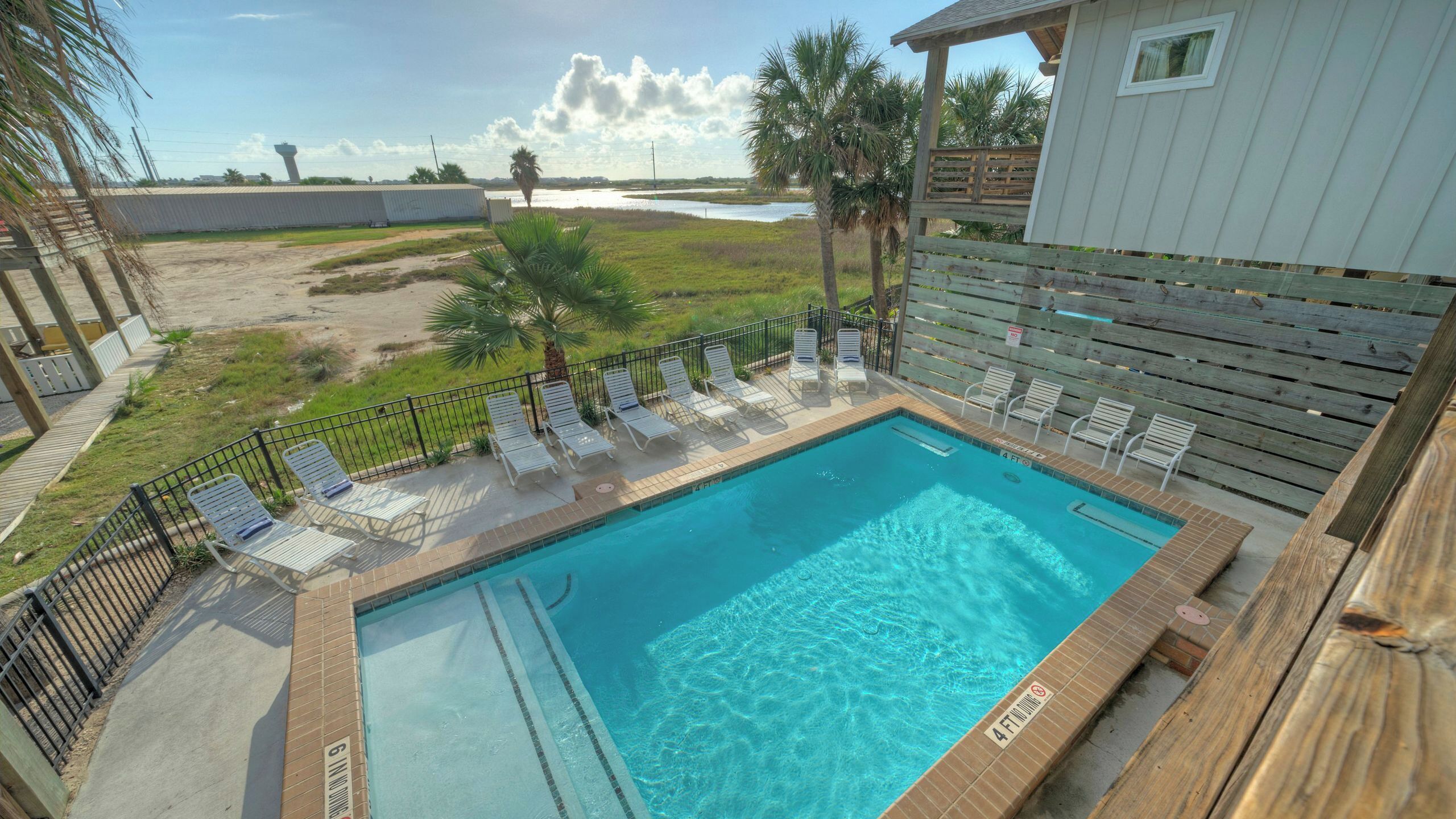 A swimming pool with lounge chairs, a wooden deck, and a view of a water body.